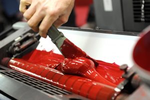 Worker uses specialized spatula to apply red paint to industrial printer | Marsid-M&M Group